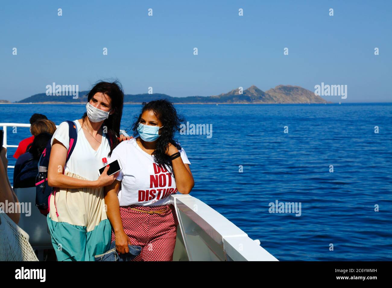 12th July 2020, Ria de Vigo, Galicia, northern Spain: Passengers wearing face masks pose for a photo on the ferry from Vigo to the Cies Islands (in background), a popular tourist destination off the coast of Galicia. Spain has relaxed travel restrictions from 21st June after a strict lockdown to control the Covid 19 coronavirus and many Spaniards are returning to the beaches. Wearing face masks is still mandatory on public transport. Stock Photo
