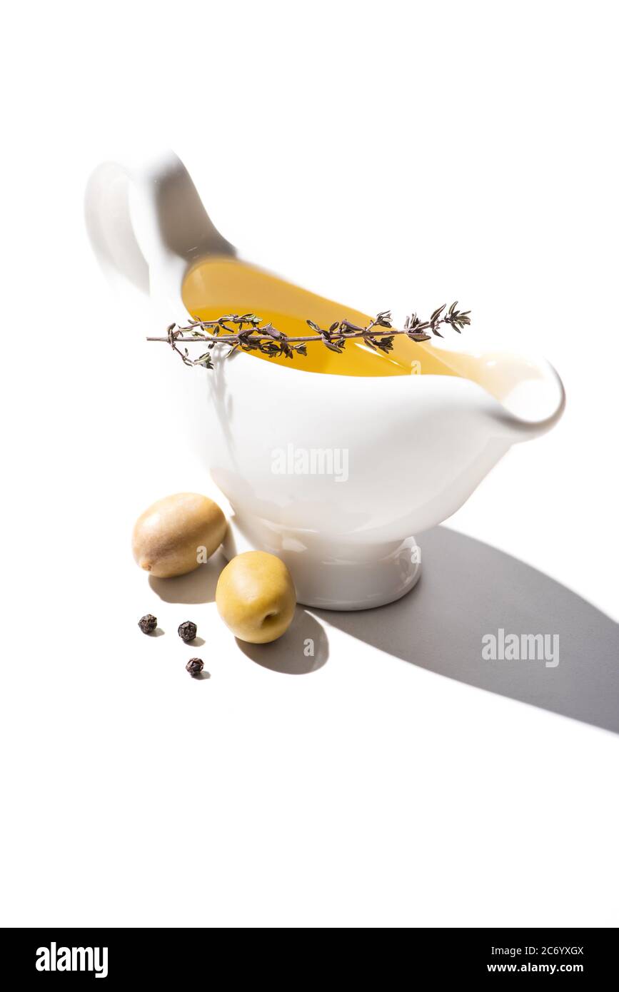 olive oil in gravy boat with herb near green olives and black pepper on