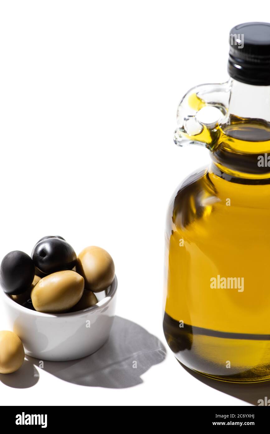 olive oil in bottle near green and black olives in bowl on white ...