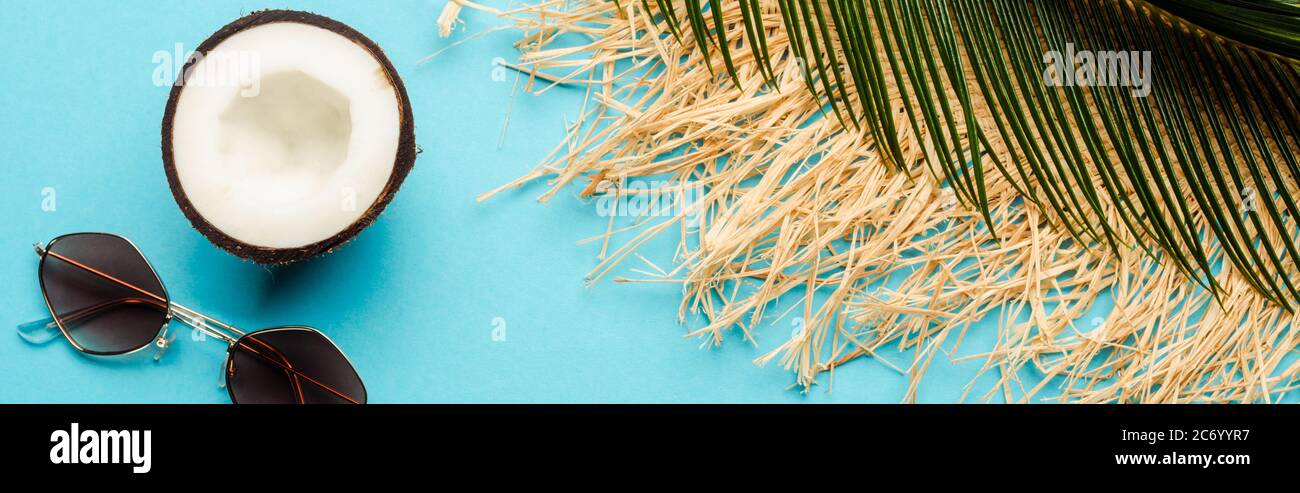 top view of green palm leaf, coconut half, sunglasses and straw hat on ...