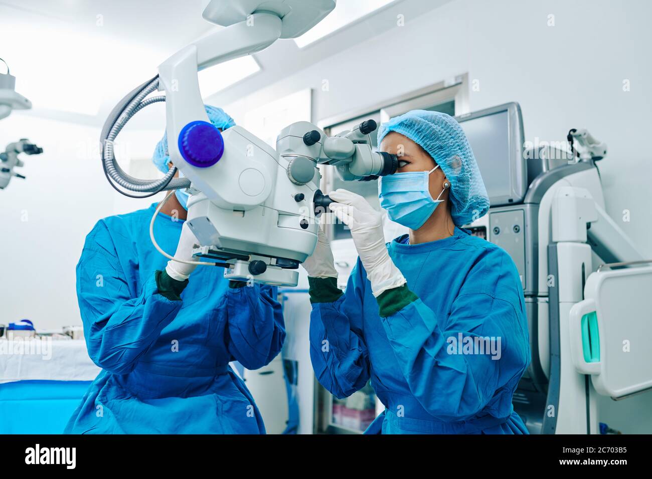 Asian female surgeon in scrubs using electronic microscope when operating patient Stock Photo