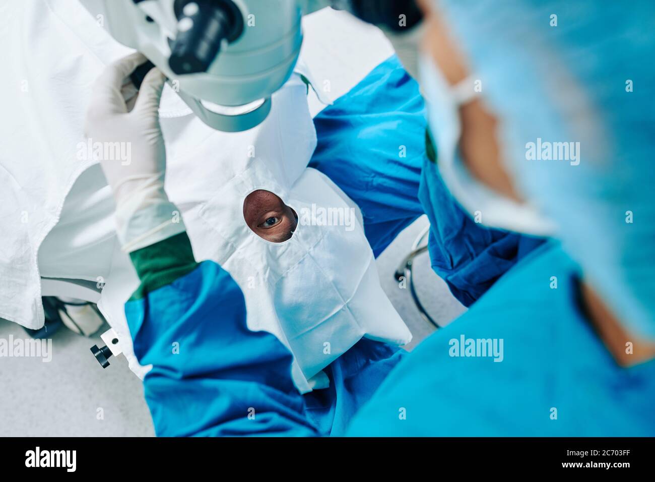 Surgical assistant installing laser equipment above patient and preparing for vision correction Stock Photo