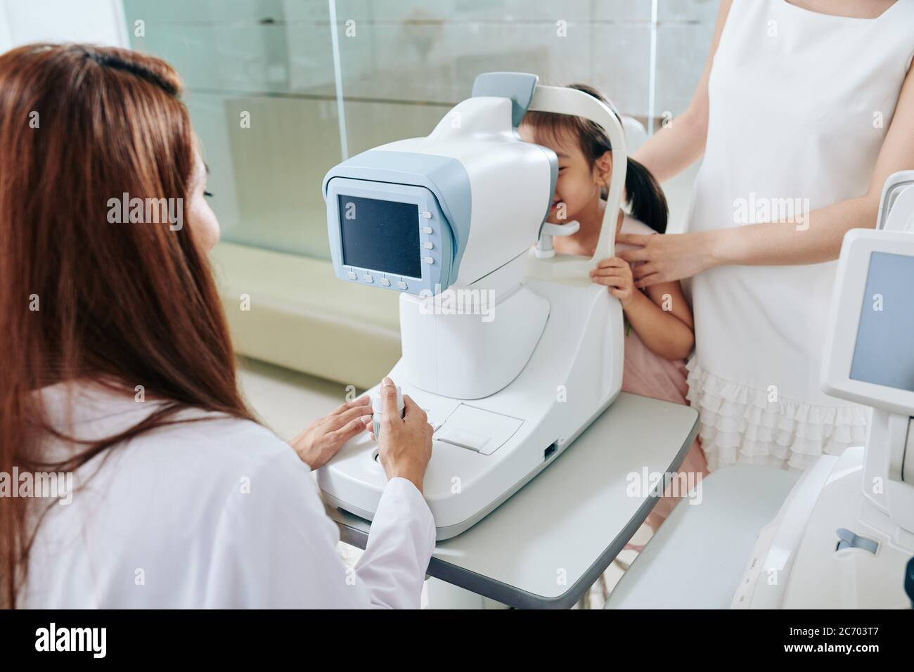 Pediatric ophthalmologist using refractometer eye test machine when checking eyesight of little