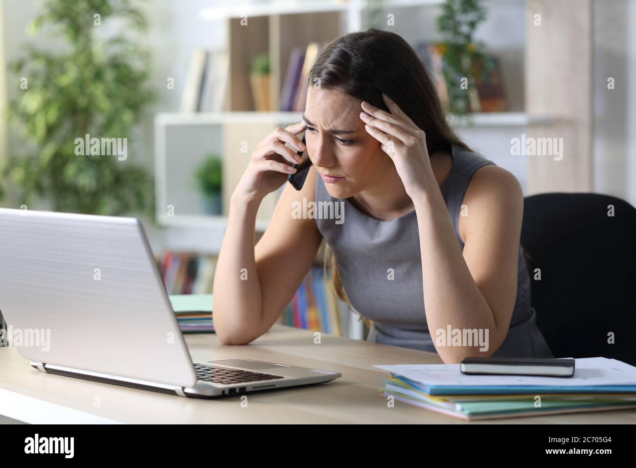 Worried entrepreneur woman calls on smart phone with laptop sitting on a desk at homeoffice Stock Photo
