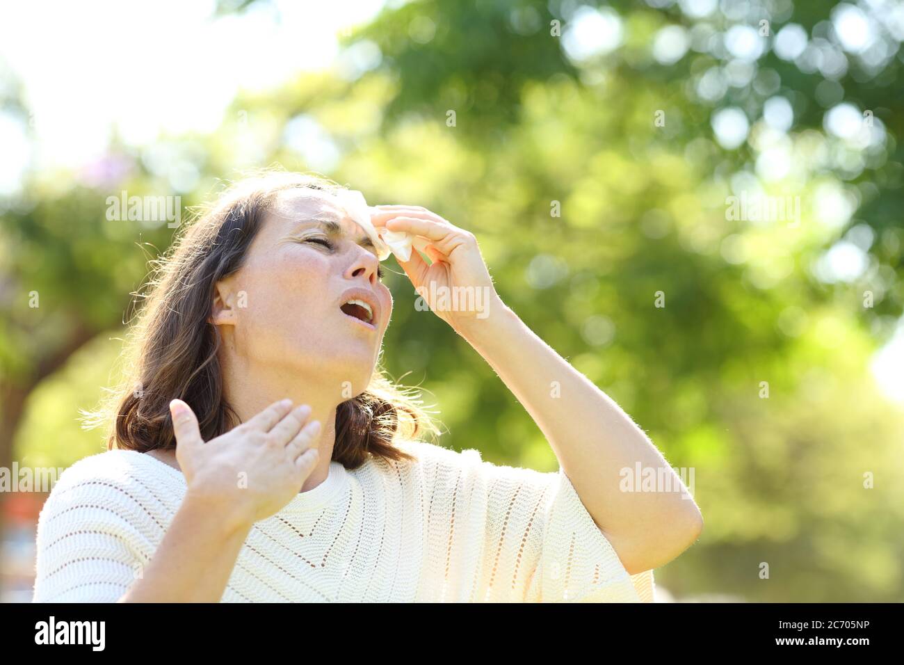 Adult woman sweating suffering heat stroke cleaning with tissue in the park Stock Photo