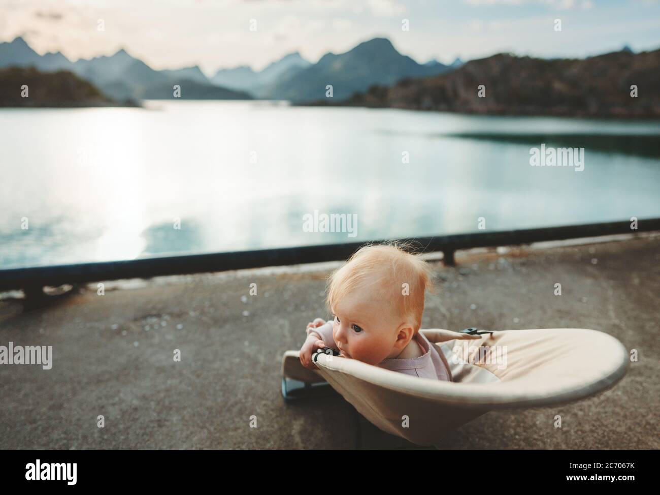 Child traveling in Norway family vacation lifestyle outdoor infant baby sitting in chair enjoying sunset mountains and fjord view Stock Photo