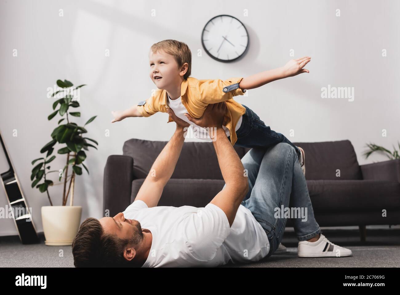 father lying in floor and holding adorabe son imitating flying with outstretched hands Stock Photo