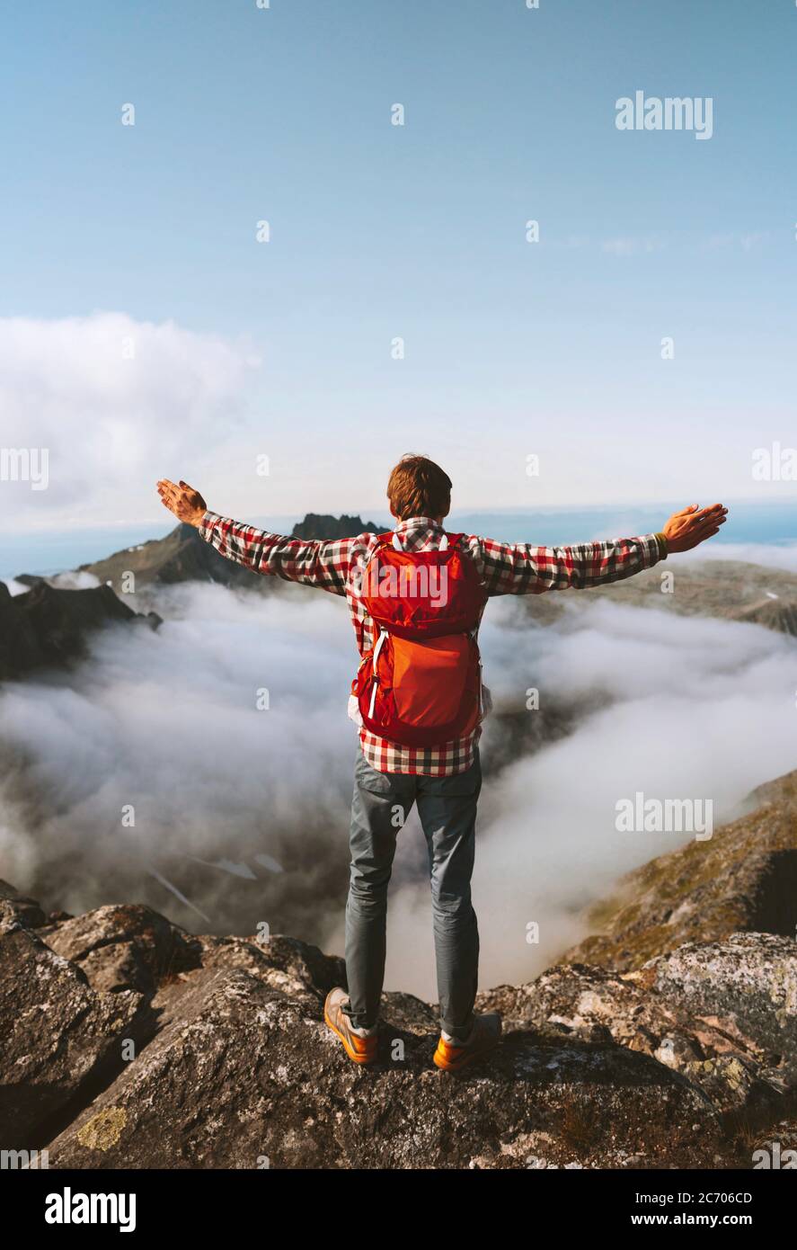 Man with backpack traveling alone hiking outdoor adventure vacation active healthy lifestyle hiker raised hands on mountain top above clouds mental he Stock Photo
