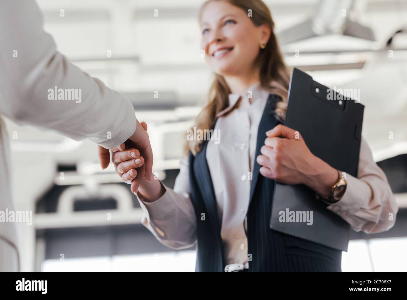 selective focus of smiling businesswoman shaking hands with coworker in office Stock Photo