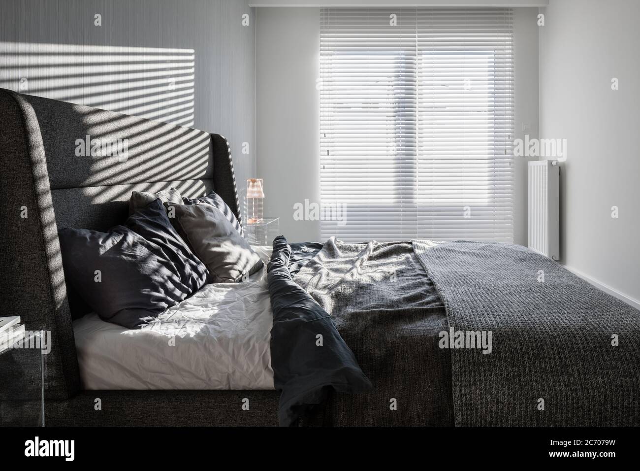 Sunny, gray bedroom with double bed and window blinds Stock Photo