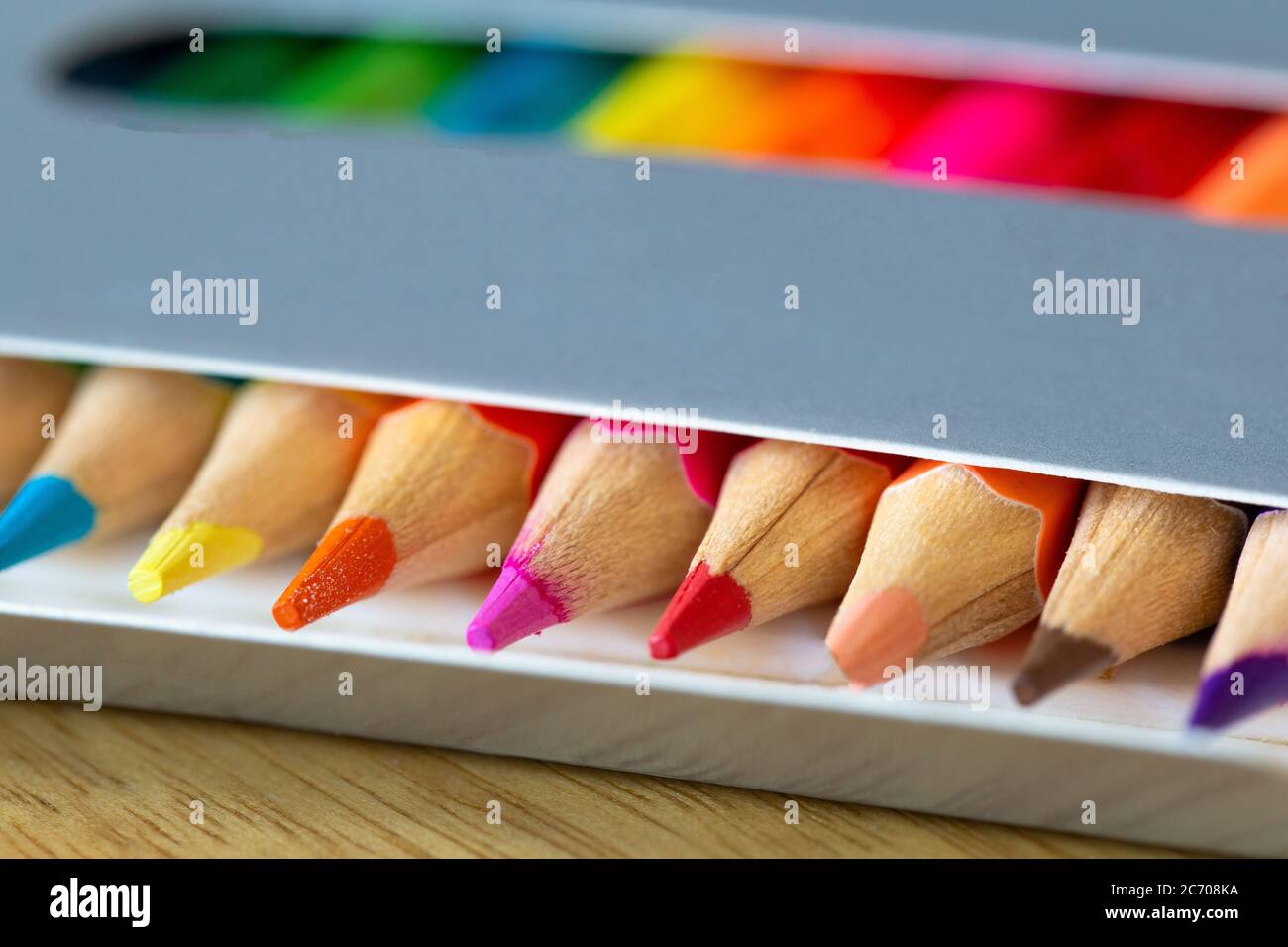 Colored pencils in a carton grey box, rainbow colors, orange pencil sticks out macro, school or