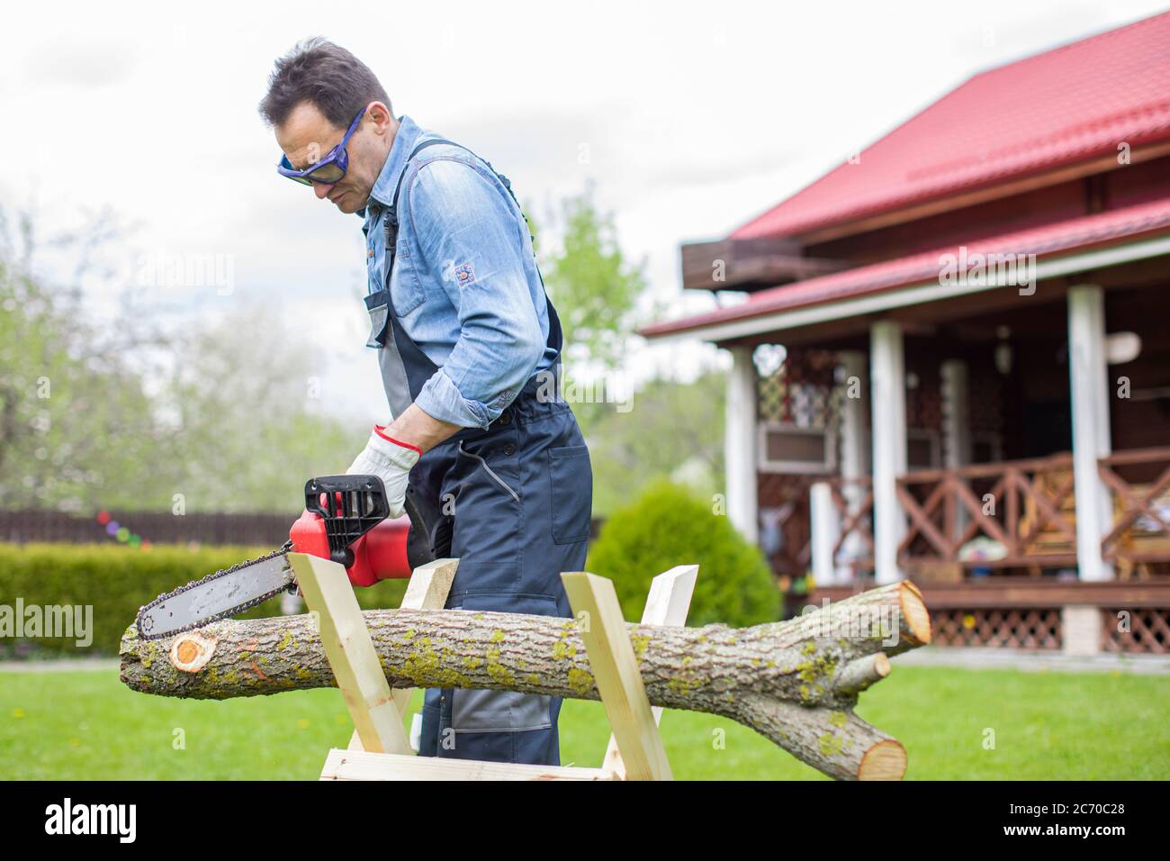 Lumberjack in working uniform sawing tree trunk on sawhorse with ...