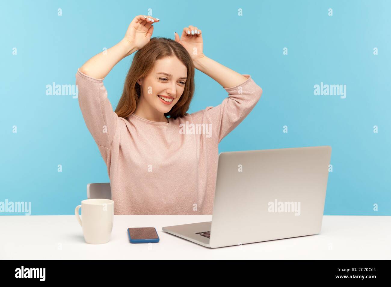 Positive playful young woman smiling and showing bunny ears on head while looking on laptop screen on video call, chatting on webcam and flirting. ind Stock Photo