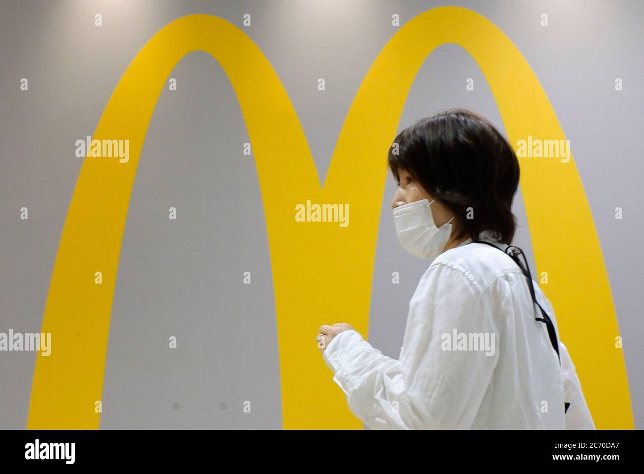 A woman wearing a protective face mask walks past a McDonald's store at a shopping district amid the coronavirus (COVID-19) outbreak.Tokyo on Monday reported 119 new coronavirus infections, falling below 200 for the first time in five days, Tokyo Gov. Yuriko Koike said. Stock Photo