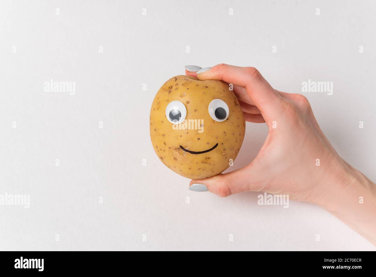 Woman's hand holding raw potatoes with funny face. Potatoes with Googly