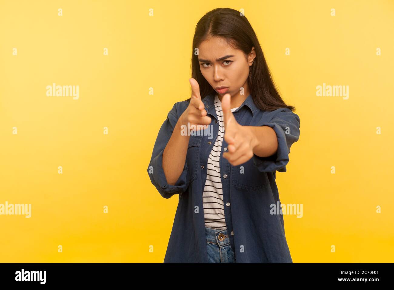 I'll shoot you! Portrait of purposeful dangerous girl in denim shirt shooting to camera with finger pistols, threatening to kill, gesturing weapon. in Stock Photo