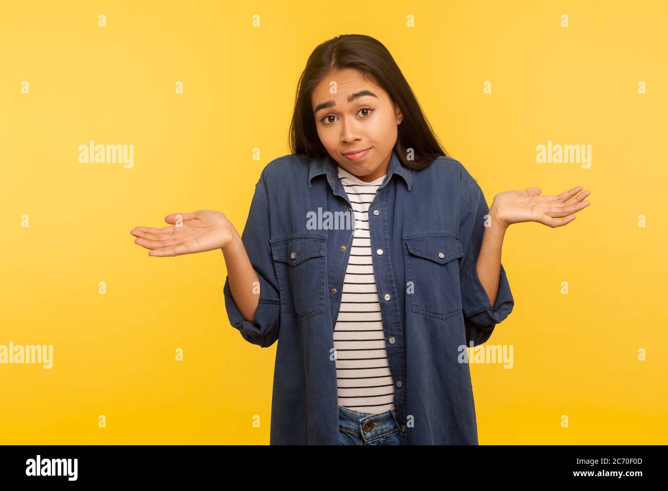 Have no idea, maybe! Portrait of confused girl in denim shirt shrugging shoulders in bewilderment, doubting and feeling uncertain, don't know answer. Stock Photo