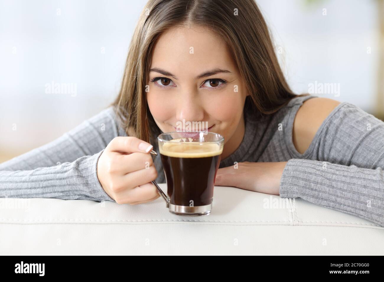Satisfied woman smelling a coffee cup looking at camera sitting in the