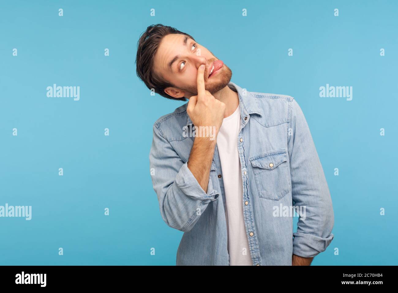 Misconduct, bad manners. Portrait of funny crazy man in worker denim shirt picking nose and sticking out tongue with dumb comical expression, fooling Stock Photo