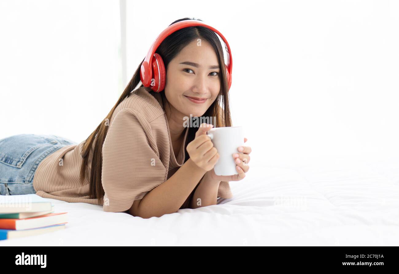 Teen wearing headphones drinking a cup of coffee relax on bed at home after reviewing the textbook. Stock Photo