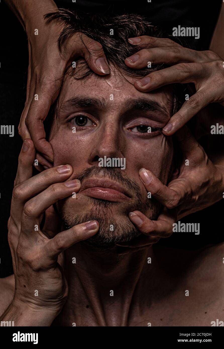Four hands distort a mans face, he appears depressed and helpless Stock Photo
