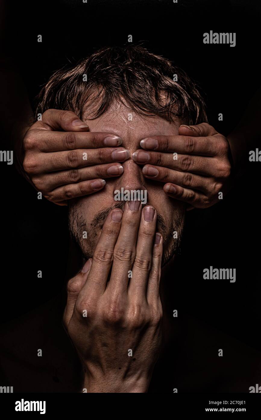Three hands cover a man's eyes and mouth, so he cannot see or speak. Stock Photo