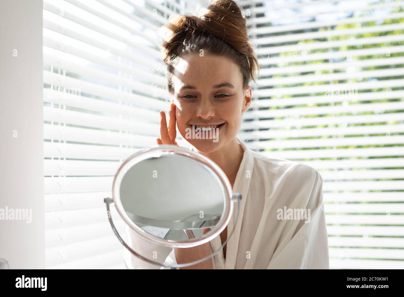 Woman touching her face while looking in the mirror Stock Photo - Alamy