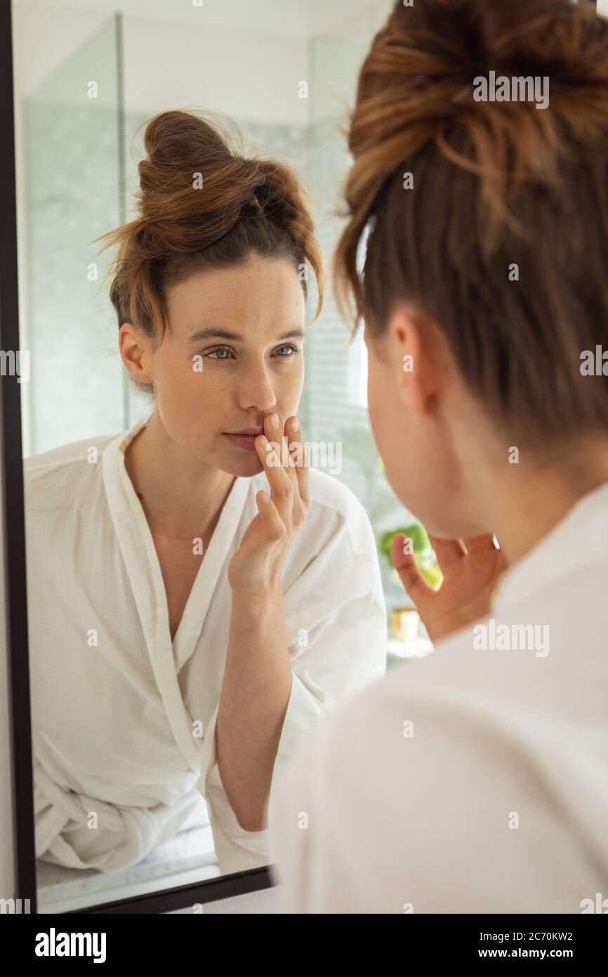 Woman touching her face while looking in the mirror Stock Photo - Alamy