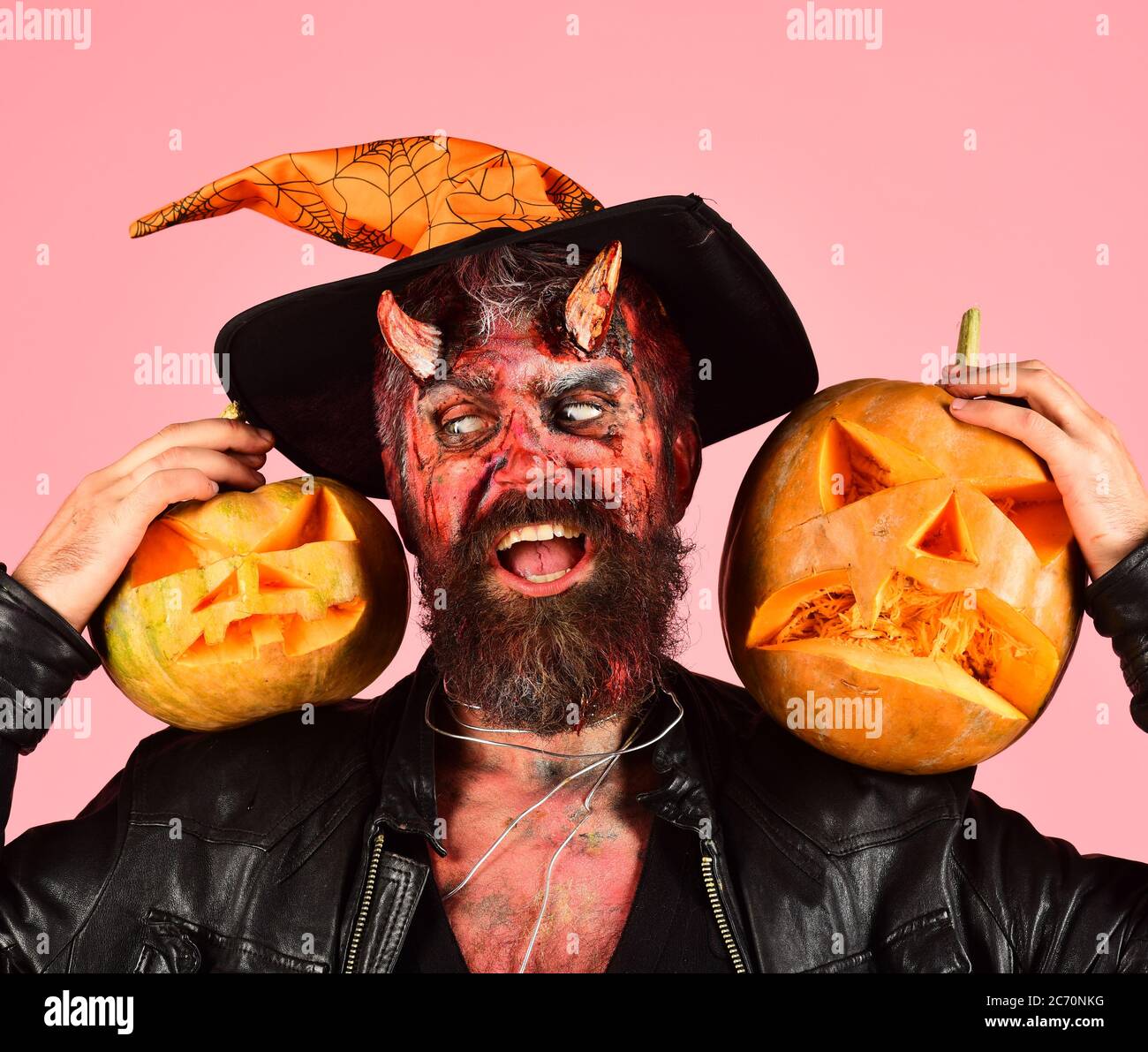 Demon with horns and suspicious face holds carved jack o lantern. Man  wearing scary makeup holds pumpkin on green background. Halloween party  concept. Devil or monster with October decorations Stock Photo -