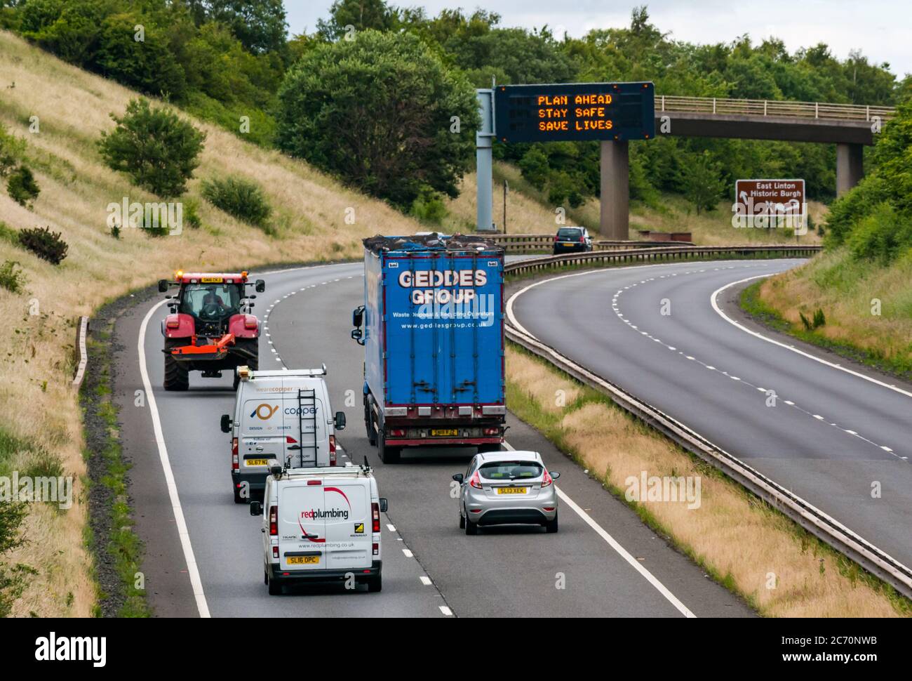 East Lothian, Scotland, United Kingdom, 13th July 2020. A1 Covid-19 travel advice as Scotland enters Phase 3 on an overhead gantry with the new iteration of the message: 'Plan Ahead, Stay Safe, Save Lives'. This is the 4th iteration of the Coronavirus slogans used by the Scottish Government during the pandemic. The dual carriageway is much busier and almost back to normals levels of traffic Stock Photo