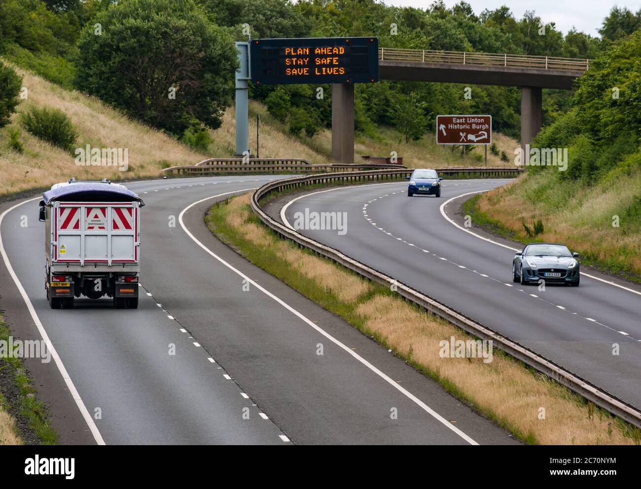 East Lothian, Scotland, United Kingdom, 13th July 2020. A1 Covid-19 travel advice as Scotland enters Phase 3 on an overhead gantry with the new iteration of the message: 'Plan Ahead, Stay Safe, Save Lives'. This is the 4th iteration of the Coronavirus slogans used by the Scottish Government during the pandemic. The dual carriageway is much busier and almost back to normals levels of traffic Stock Photo