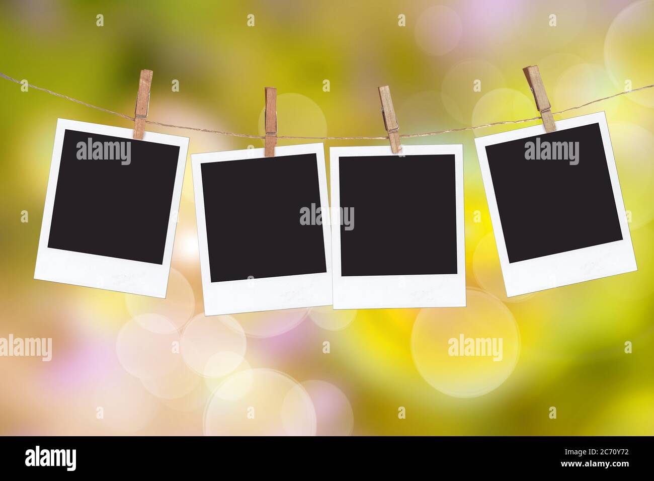 Four blank instant photo frames hanging on a rope, on green blur nature