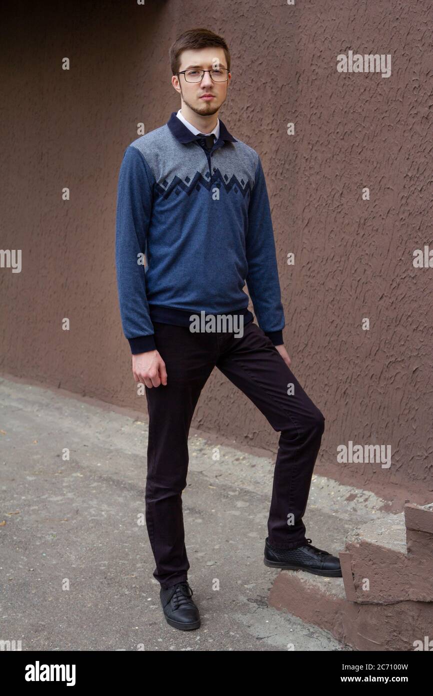 Portrait of stylish brunet young man, wearing blue jumper, standing on a city street Stock Photo