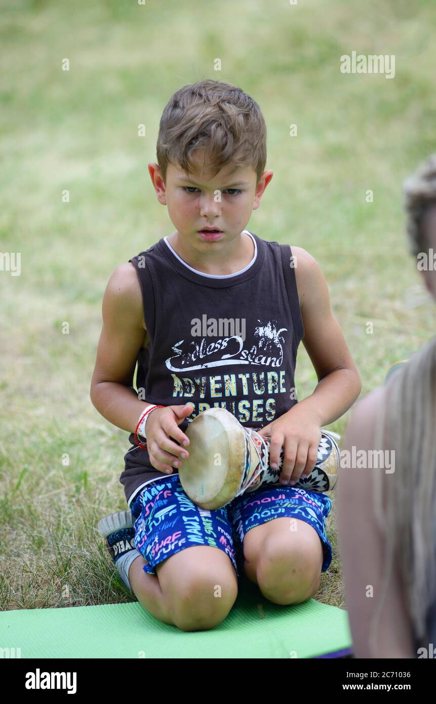 Little boy playing children doumbek sitting on the grass at the city