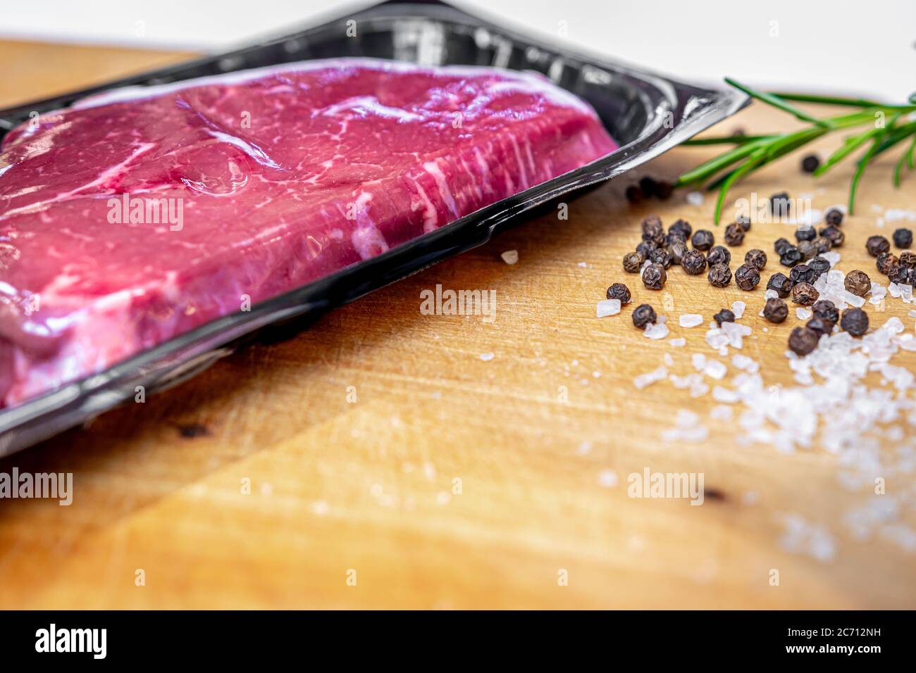 Beef steak in vacuum skin packaging and spices on wooden chopping board with copyspace Stock Photo