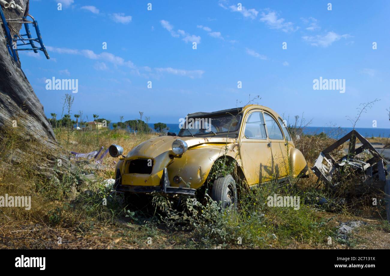 Abandoned gold coloured Citroen 2cv car wreck, Northern Cyprus with blue sky on waste ground copy space with ocean in background Stock Photo