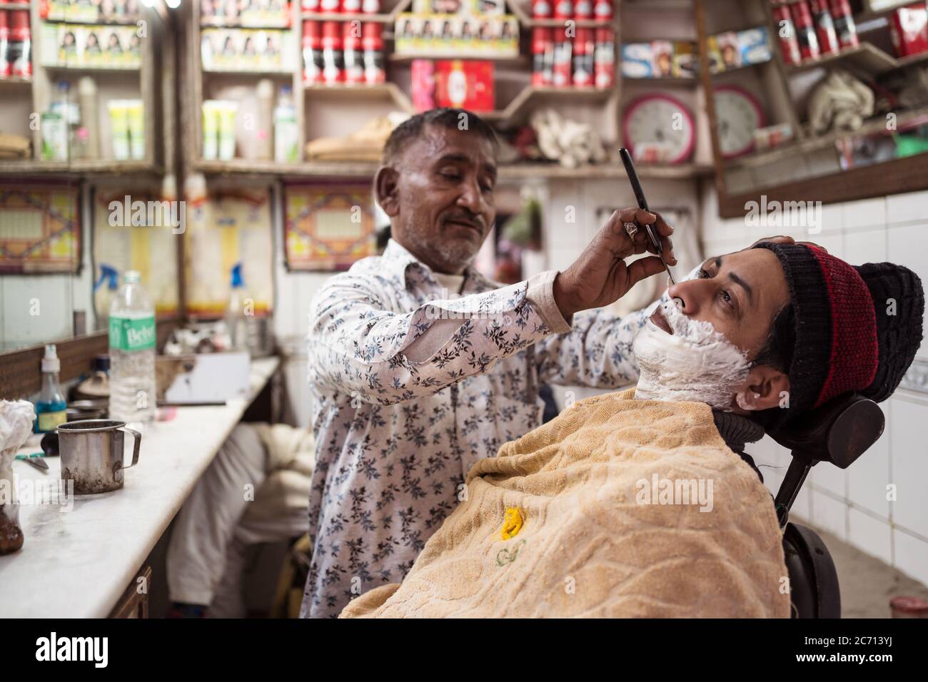 New Delhi / India - February 18, 2020: Indian barber shaving client in small barbershop in Old Delhi Stock Photo