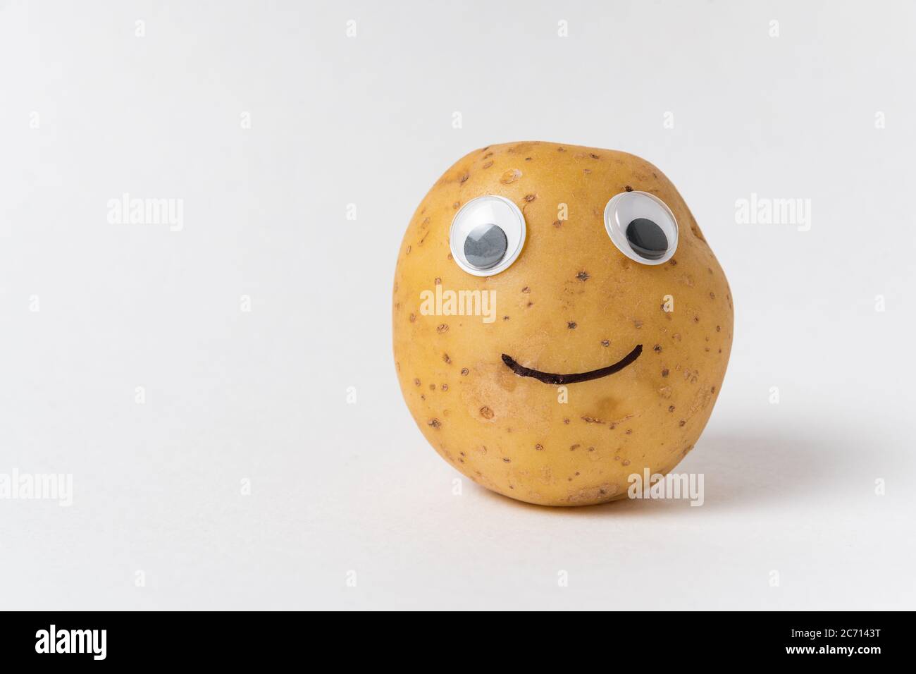 Funny raw potatoes with Googly eyes and smile on white background. Food with funny face Stock