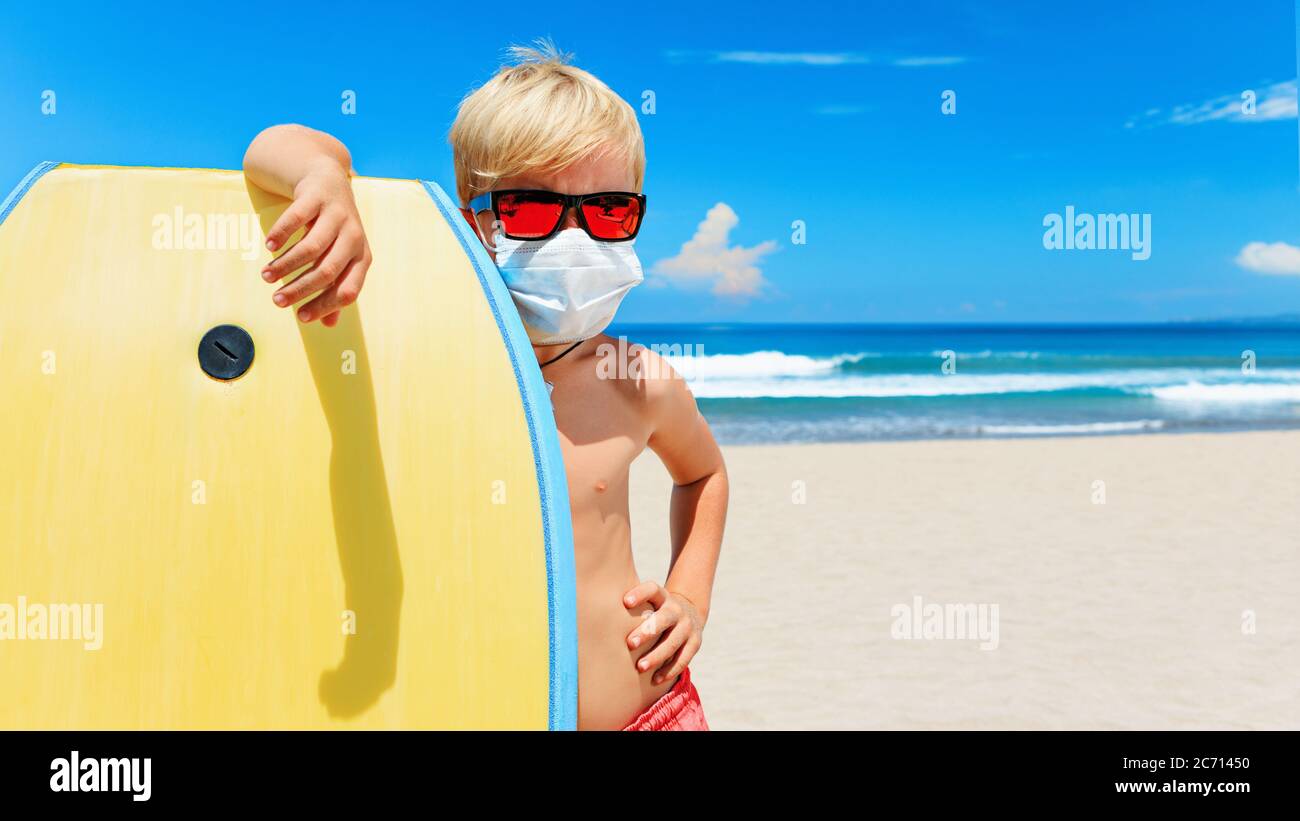 Young surfer wearing sunglasses, protective mask on sea beach with body board. Summer tours, cruises cancellation due to coronavirus COVID-19 epidemic Stock Photo