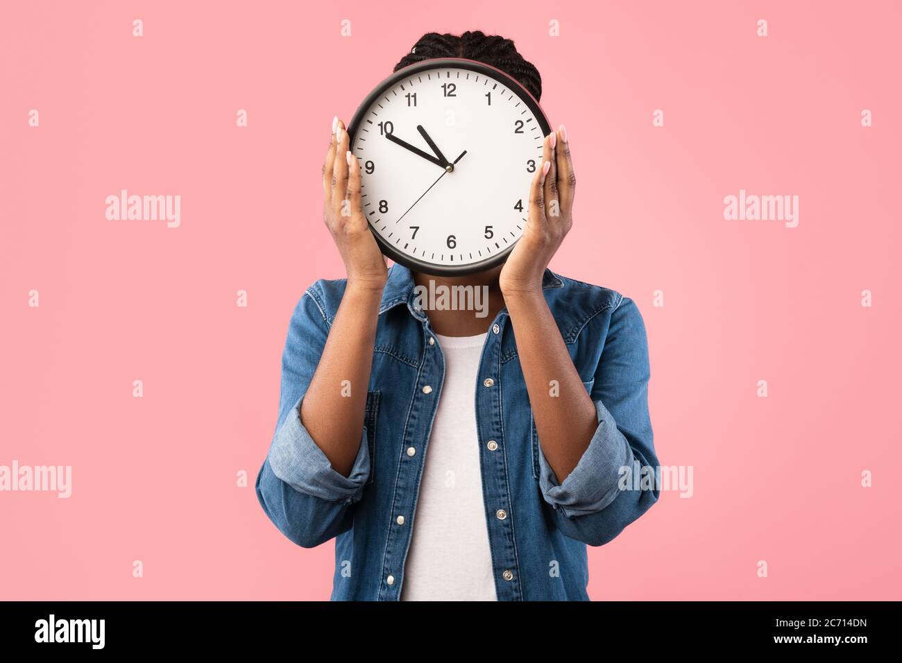 African Girl Holding Clock In Front Of Face, Pink Background Stock Photo