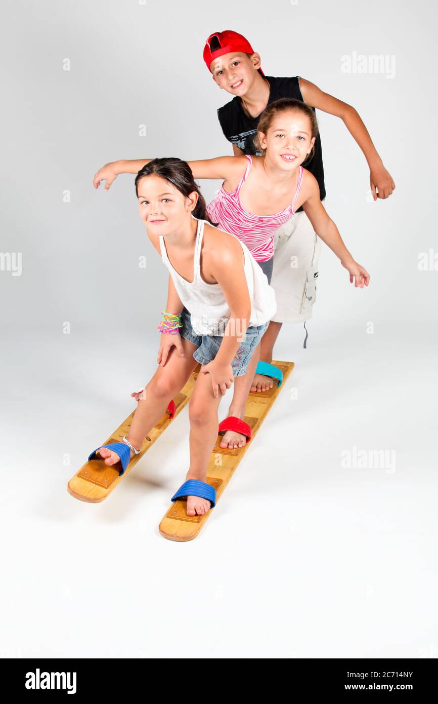 Indoor playground  3 children aged 8-12 attempt to walk together on wooden walking skies On white Background Stock Photo