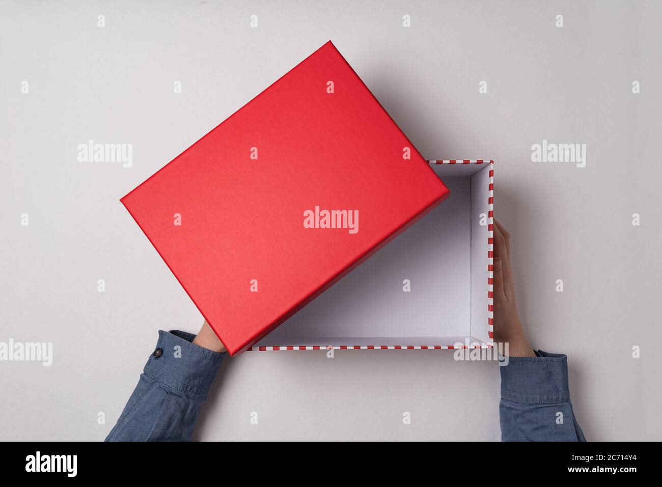 Open empty red box in children's hands on white background. Top view ...