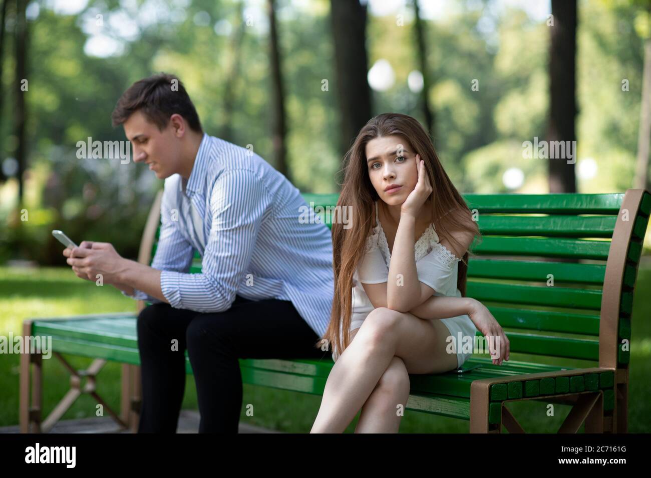 Bored young woman on dull date, suffering from her boyfriend's neglect or smartphone addiction at park Stock Photo