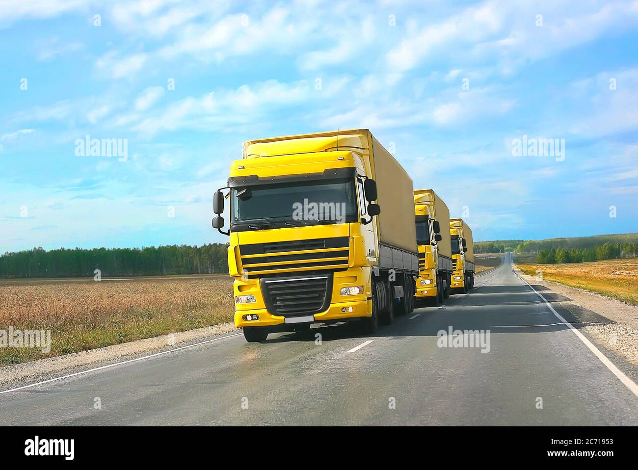 escort of yellow trucks on country road Stock Photo