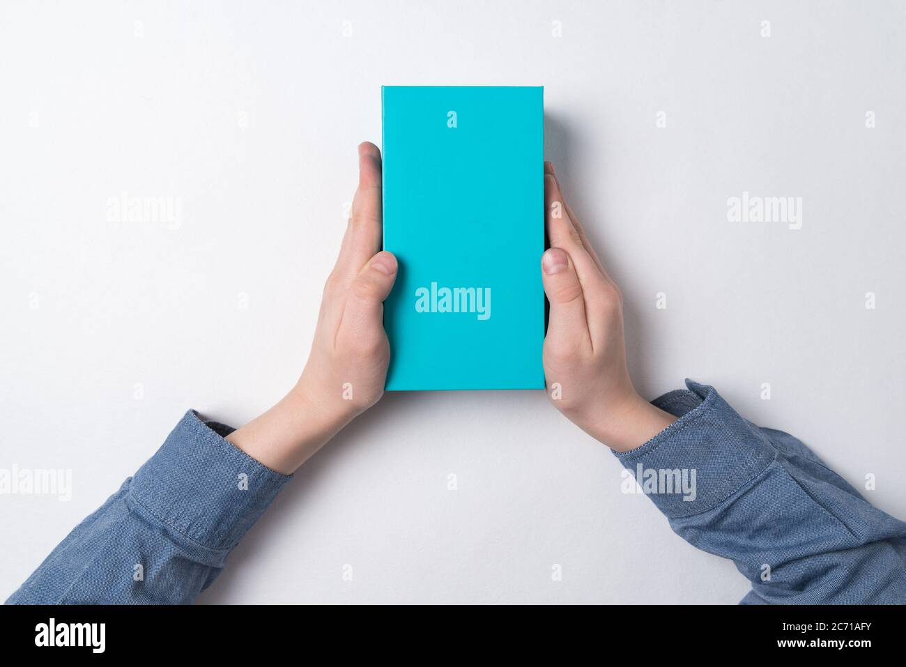 Child holds rectangular blue box on white background. Top view. Gift for child. Stock Photo
