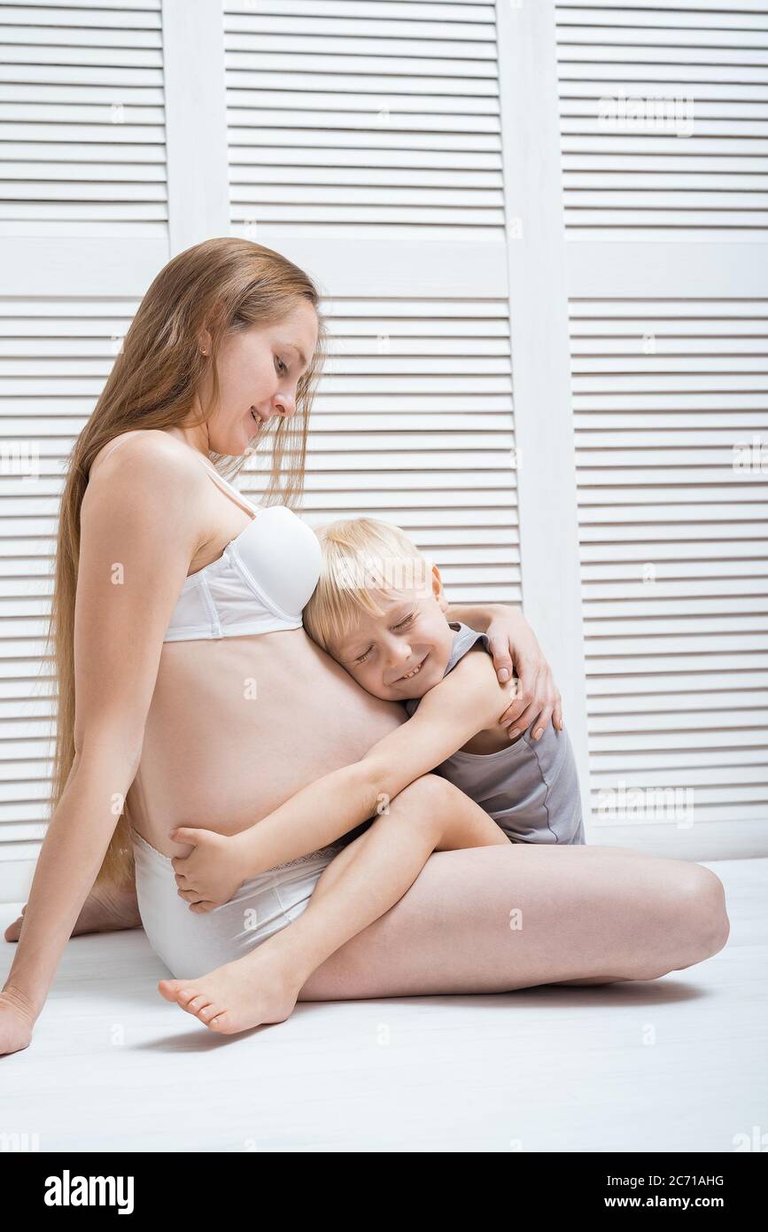 eldest son hugging his pregnant mom. Beautiful young pregnant woman and  child sit on floor. Vertical frame Stock Photo - Alamy