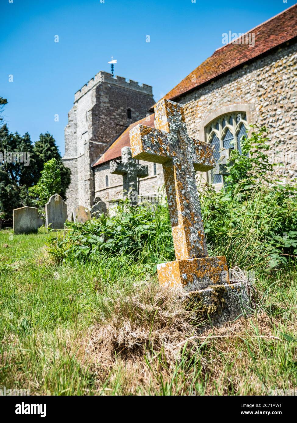 Overgrown English church yard. A view of a typical old English church with the foreground dominated by a long forgotten crucifix grave stone. Stock Photo