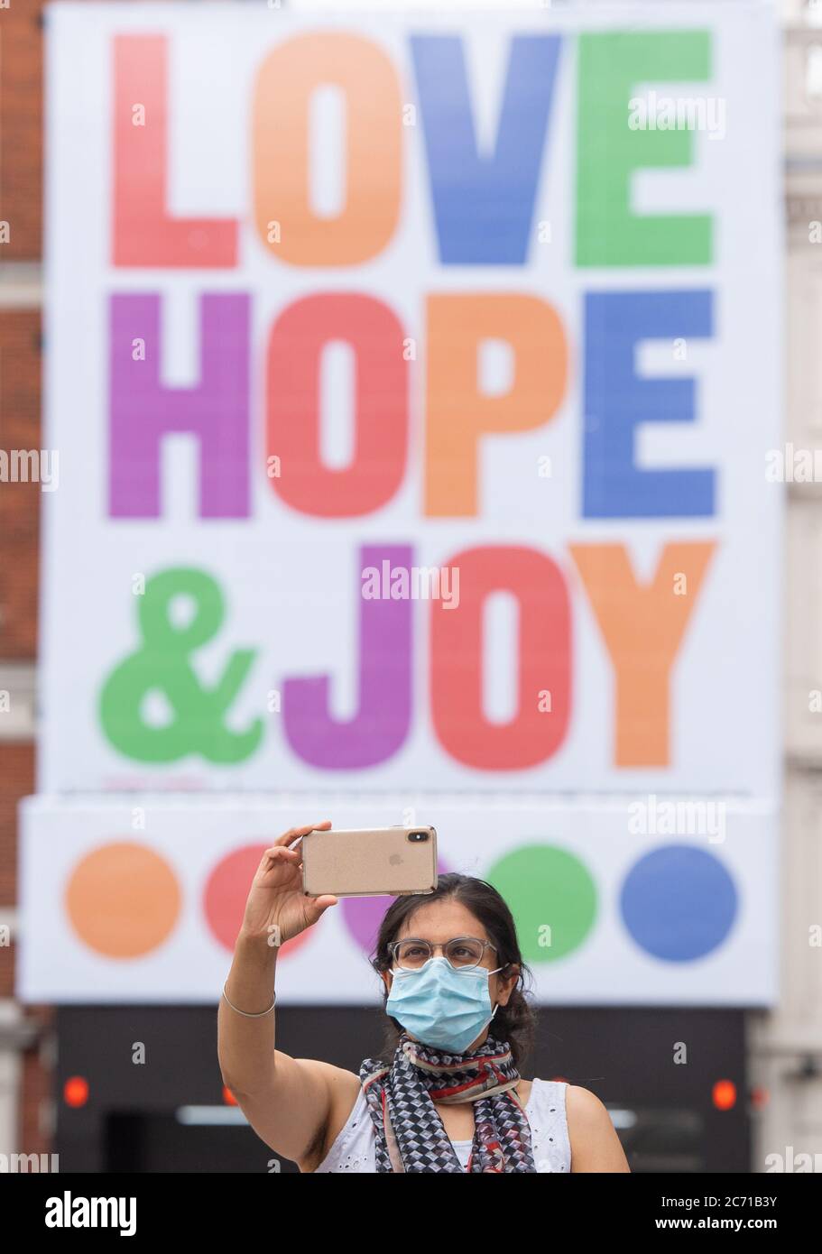 A woman wearing a protective face mask takes a selfie infront of a mural by graphic artist Anthony Burrill, in Covent Garden, London, after the lifting of further coronavirus lockdown restrictions in England. Stock Photo