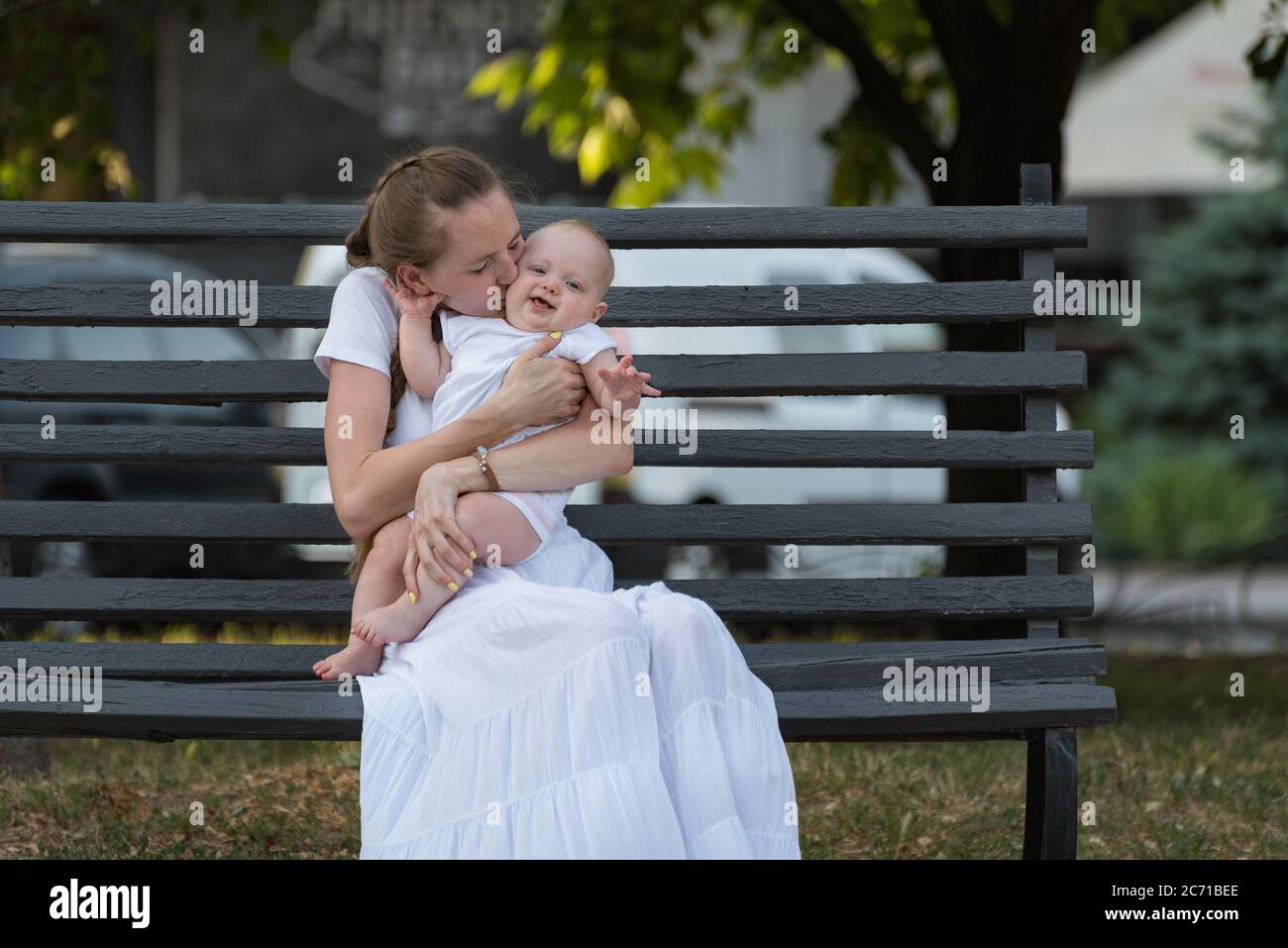 Portrait of happy mother with cute little baby sitting on bench in Park ...