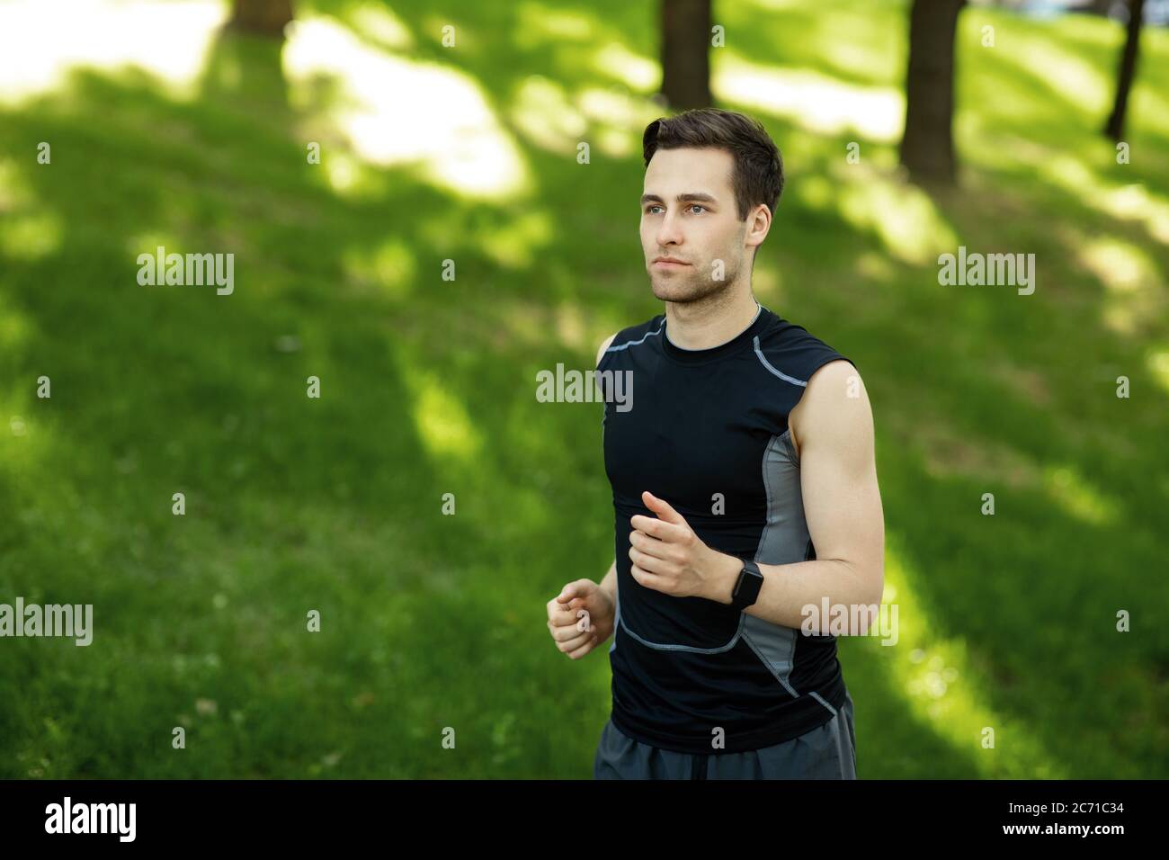 Summer sport. Guy in sportswear with fitness tracker runs in park Stock Photo